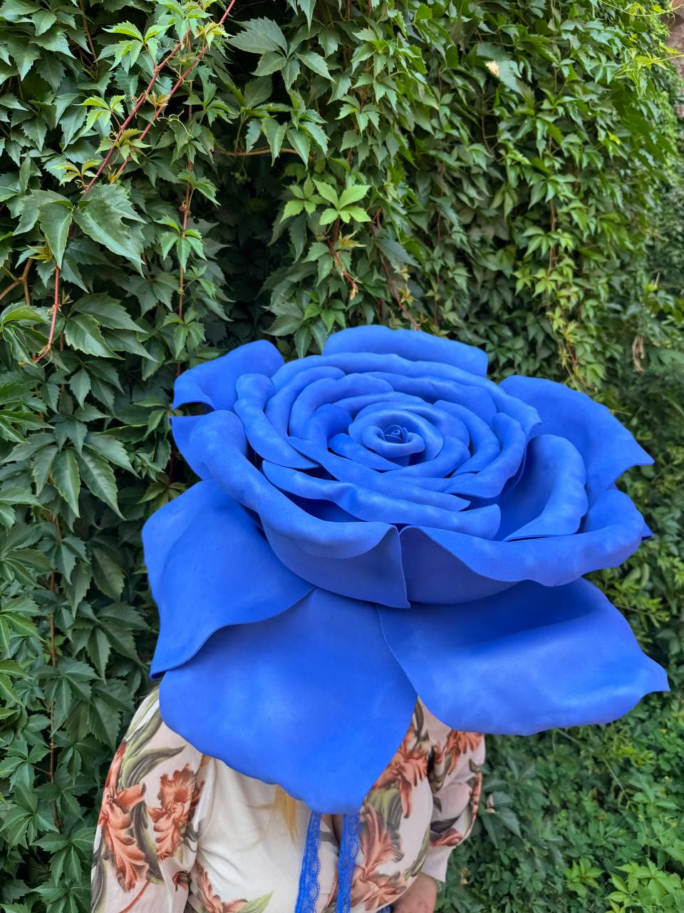 May include: A large, oversized artificial blue rose with layered, rounded petals. The flower is vibrant blue in color and features a dense, full bloom structure with a central core. The petals have a smooth, matte texture and are arranged in a circular pattern.