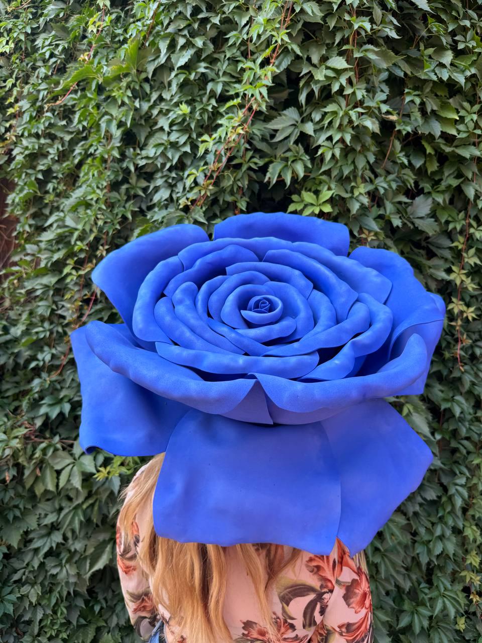 May include: A large, oversized artificial rose in a vibrant shade of blue, featuring multiple layers of rounded, smooth petals that form a dense, full bloom. The flower is positioned centrally, displaying a deep, saturated color throughout its structure.