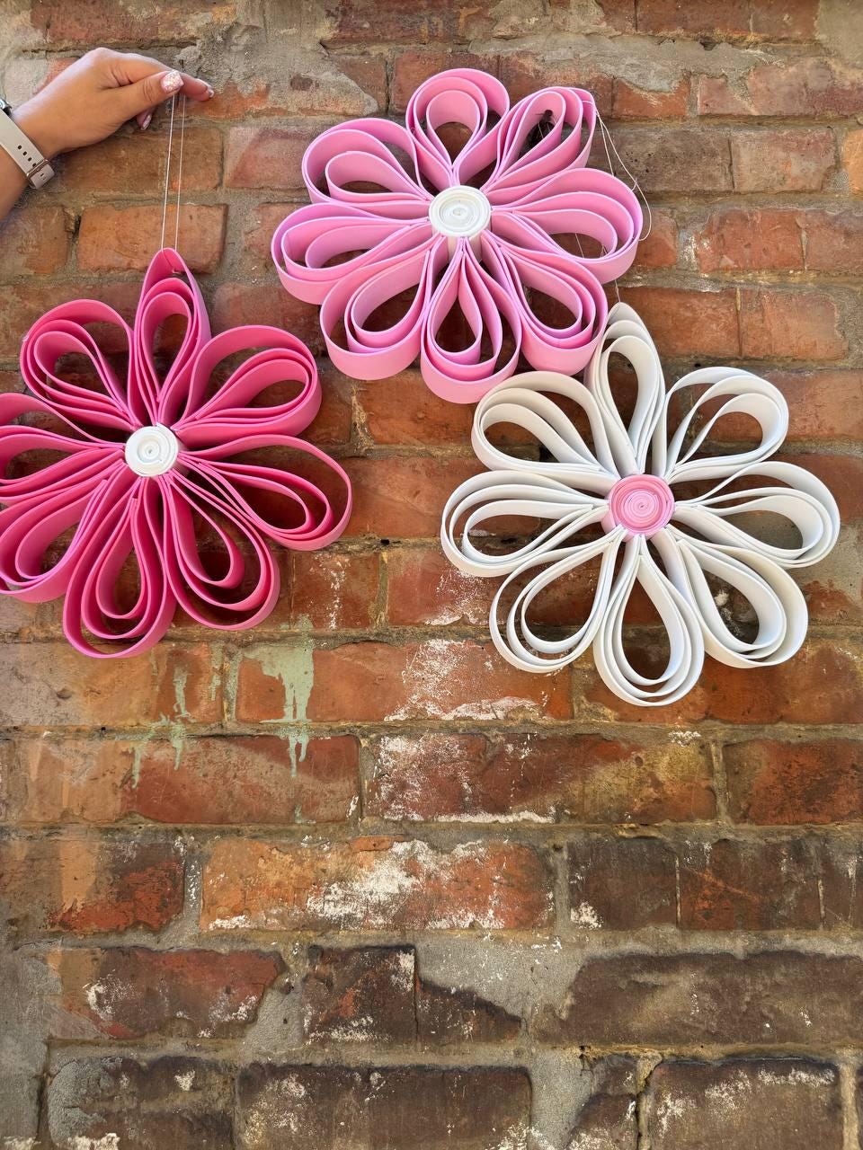 May include: Three decorative flower ornaments made from looped strips of material. Two flowers are pink with white centers, and one flower is white with a pink center. Each flower features multiple rounded petals arranged in a circular pattern.