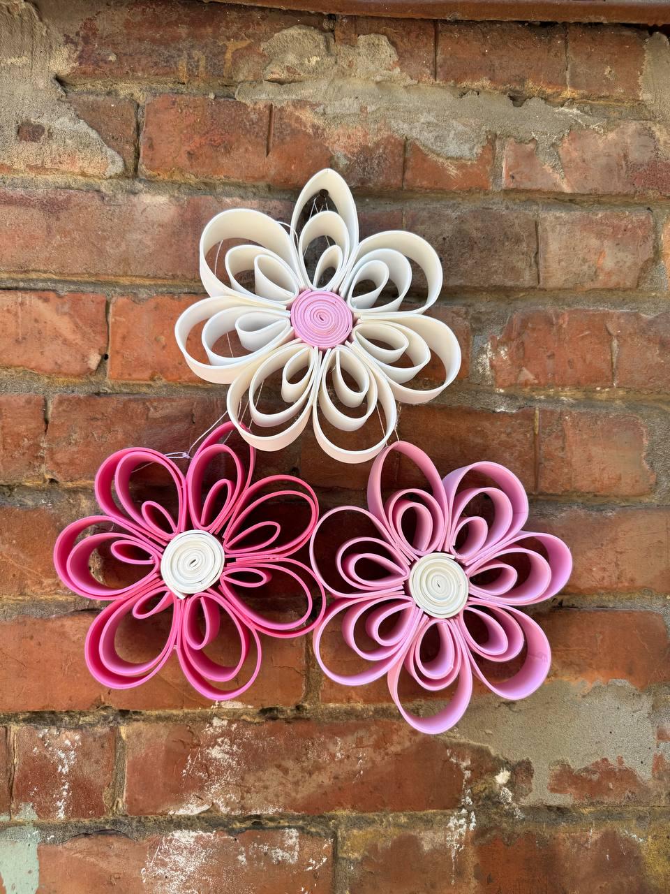 May include: Three decorative flowers crafted from looped paper strips. The top flower is white with a pink center. The bottom left flower is dark pink with a white center. The bottom right flower is light pink with a white center.