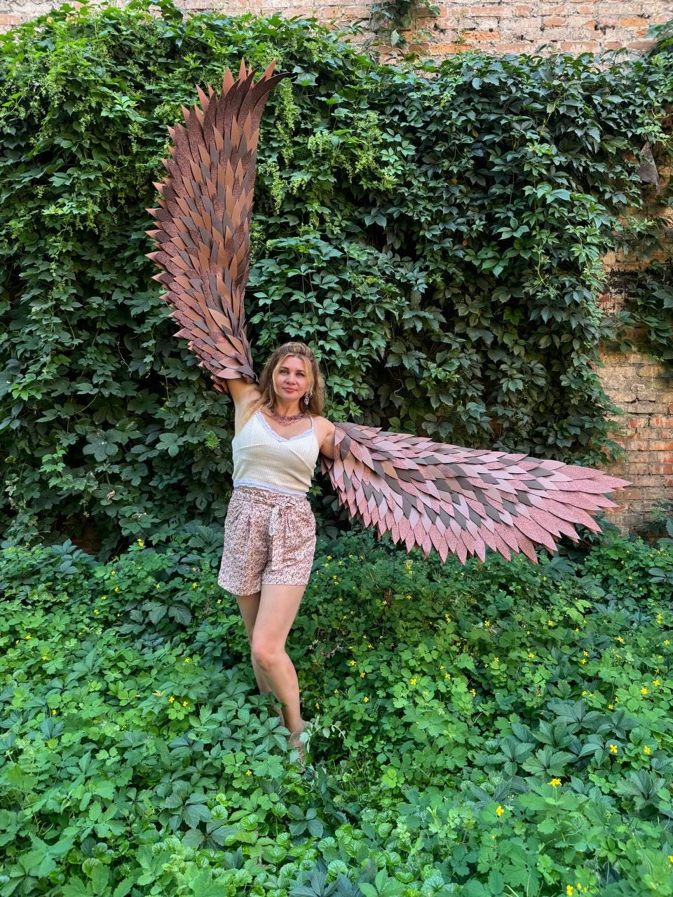 May include: A pair of large, articulated wings featuring layered, feather-like segments in shades of brown and copper. The wings are designed to be worn on the back, with one wing extended vertically and the other extended horizontally to the side.