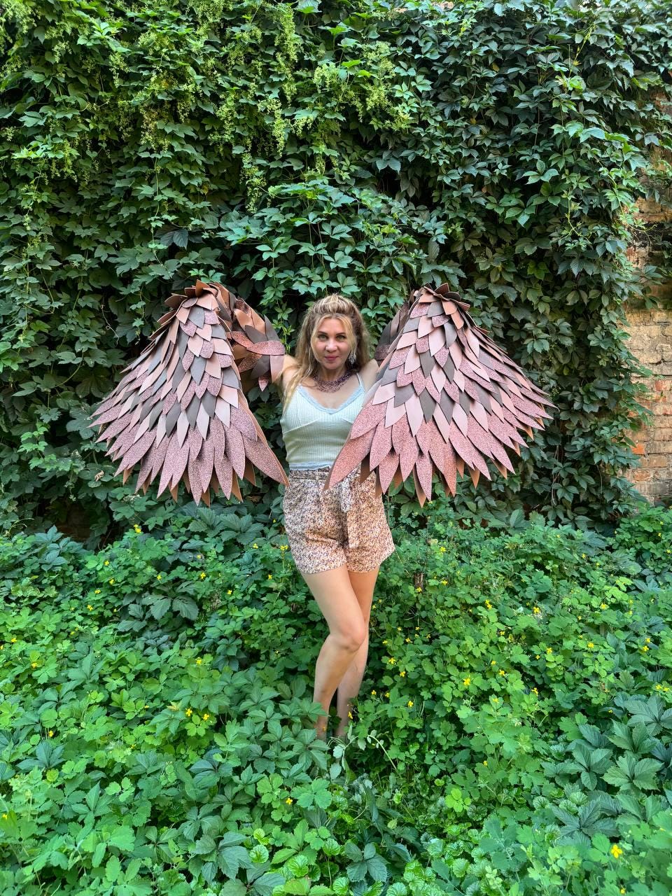 May include: A pair of large, articulated wings featuring layered, pointed feathers in shades of metallic copper and bronze. The wings are designed to be worn on the back, with a structured frame supporting the overlapping, textured feather-like panels.