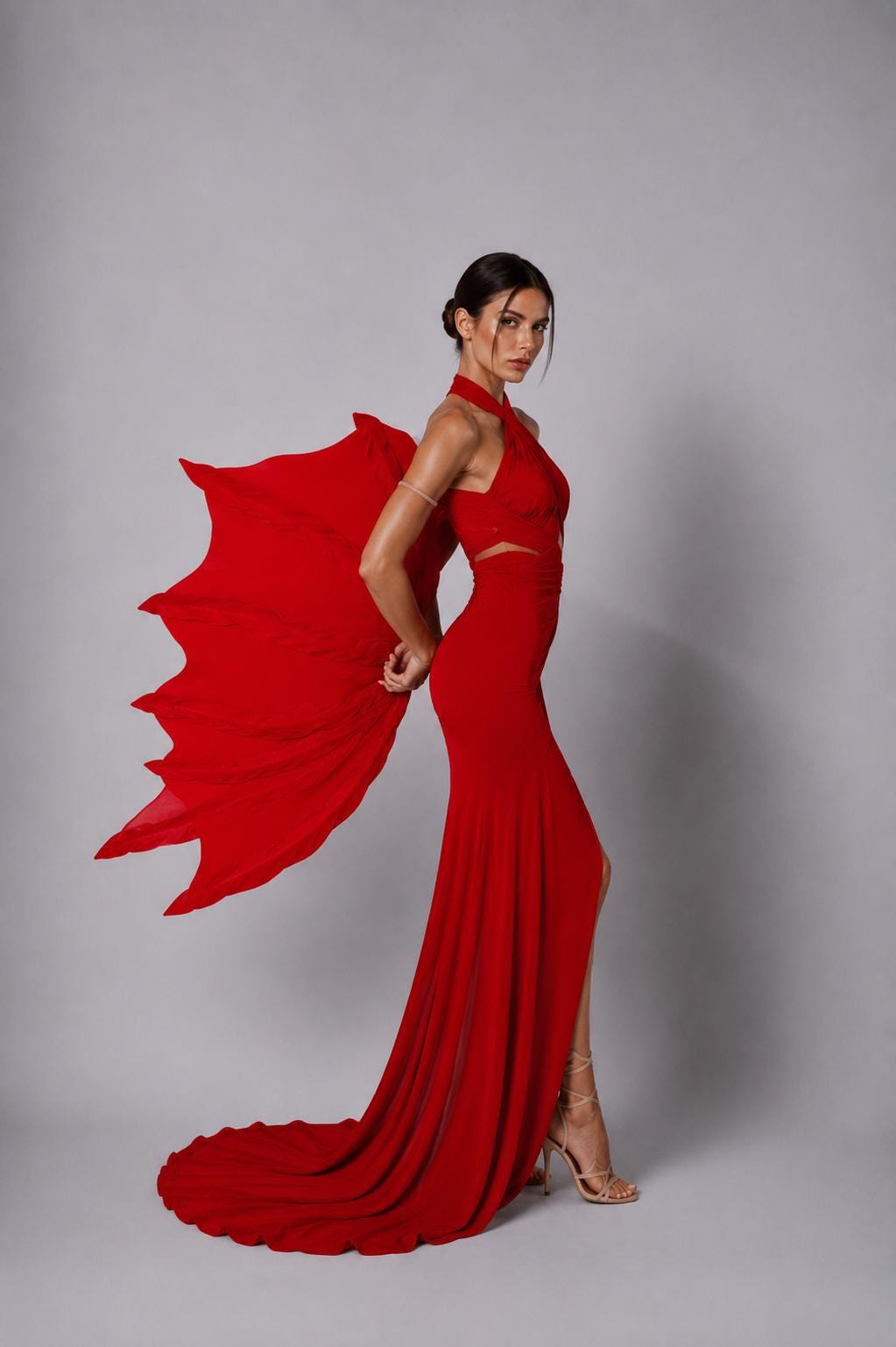 May include: A floor-length red gown featuring a halter neckline, a side slit, and a cutout at the waist. The dress includes large, wing-like fabric attachments extending from the back, creating a dramatic silhouette with a long, flowing train.