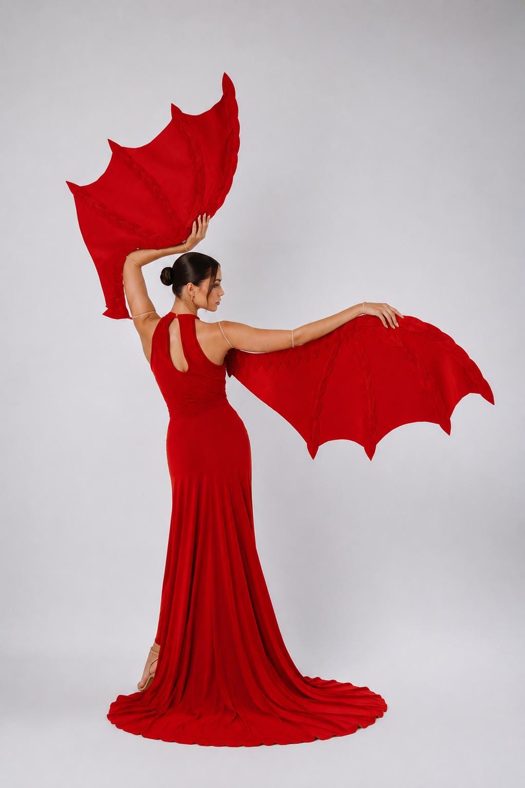 May include: A floor-length red dress with a high neckline and a keyhole cutout at the back, paired with large, articulated red dragon wings. The wings are held extended by the arms, featuring a pointed, bat-like structure with visible stitching.
