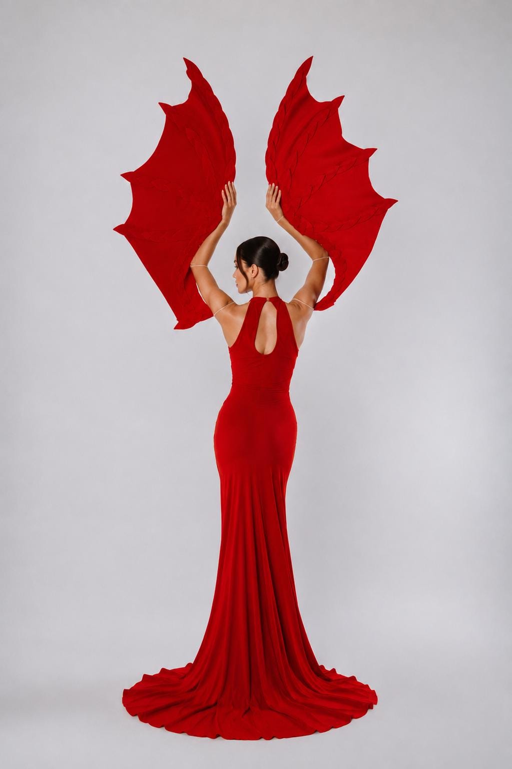May include: A floor-length red gown with a high neckline and a keyhole cutout at the back. The garment is paired with large, articulated red dragon wings that extend upward, attached to the arms with thin, transparent straps for a dramatic effect.