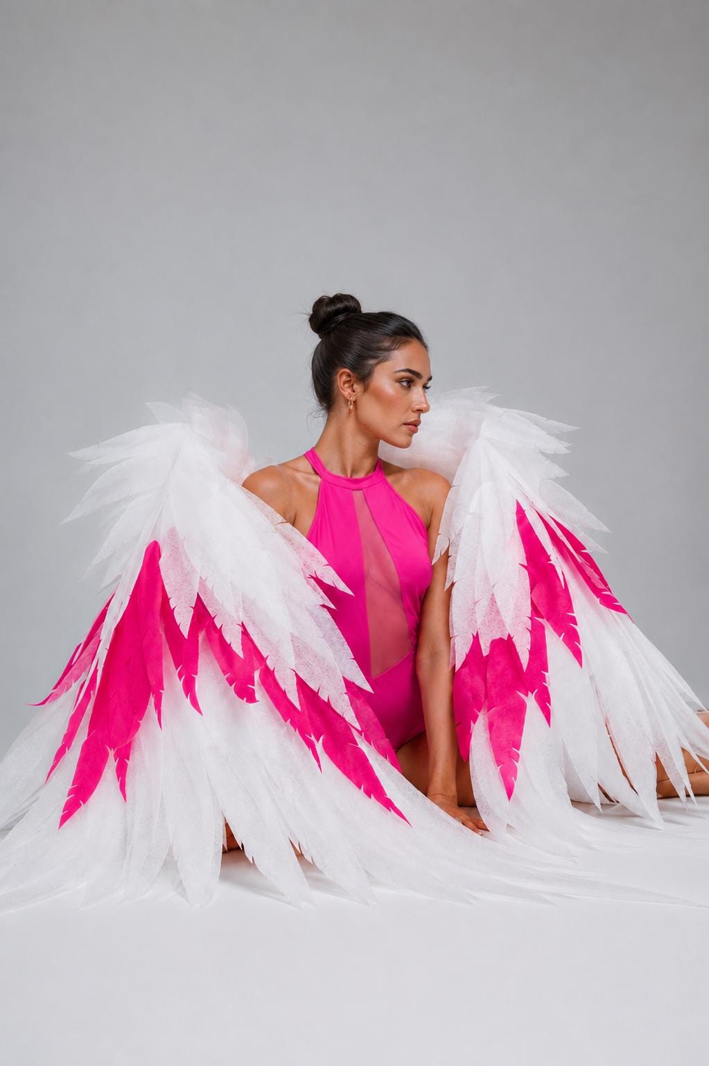 May include: Large decorative wings featuring layered white and vibrant hot pink feathers. The wings are constructed with a structured frame and a wide span, showcasing a gradient effect where the white feathers transition into bold pink accents.