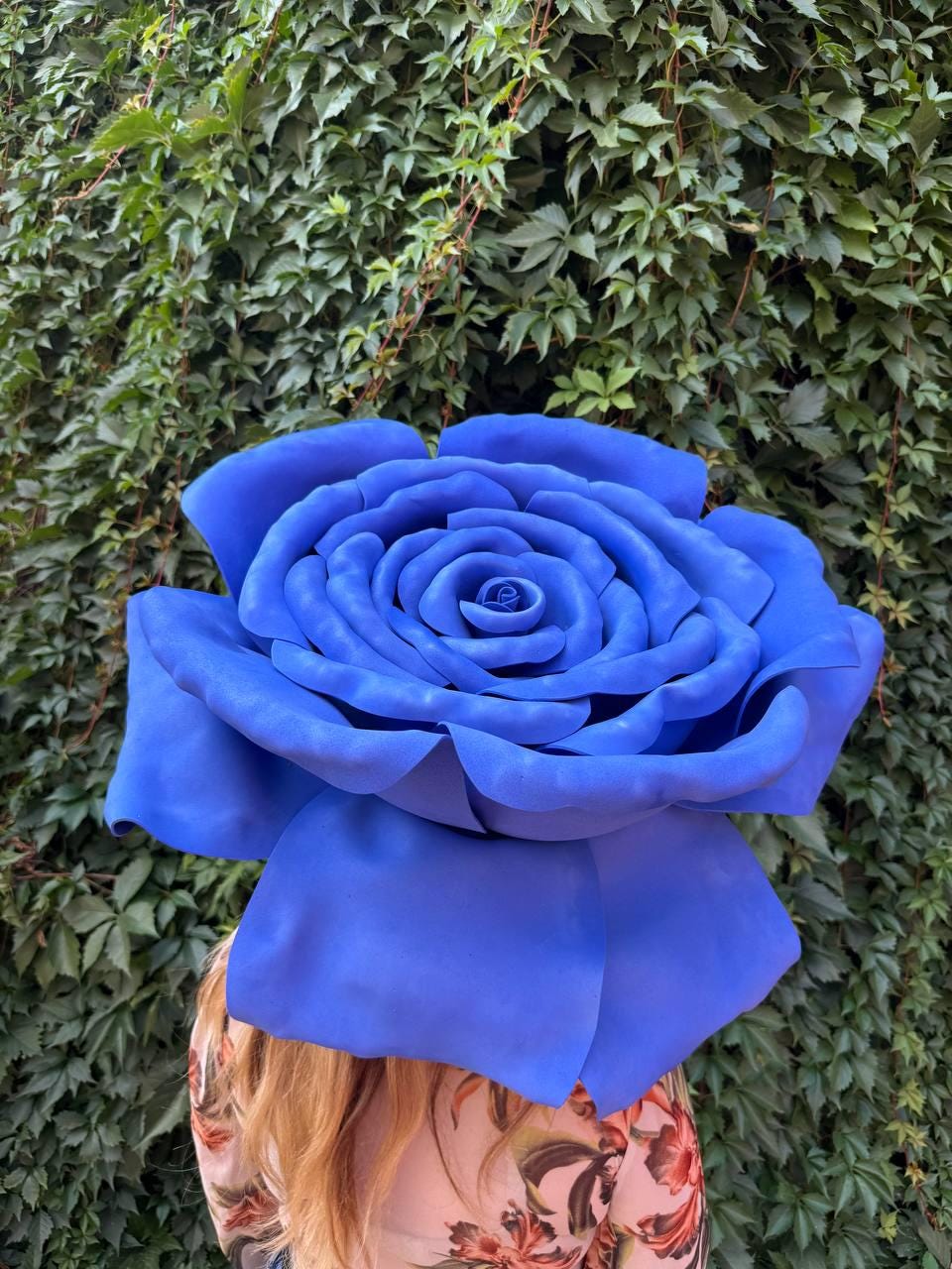 May include: A large, oversized artificial rose in a vibrant shade of blue. The flower features multiple layers of curved, smooth petals that spiral toward a tight center, creating a full, rounded bloom with a matte texture and consistent color.