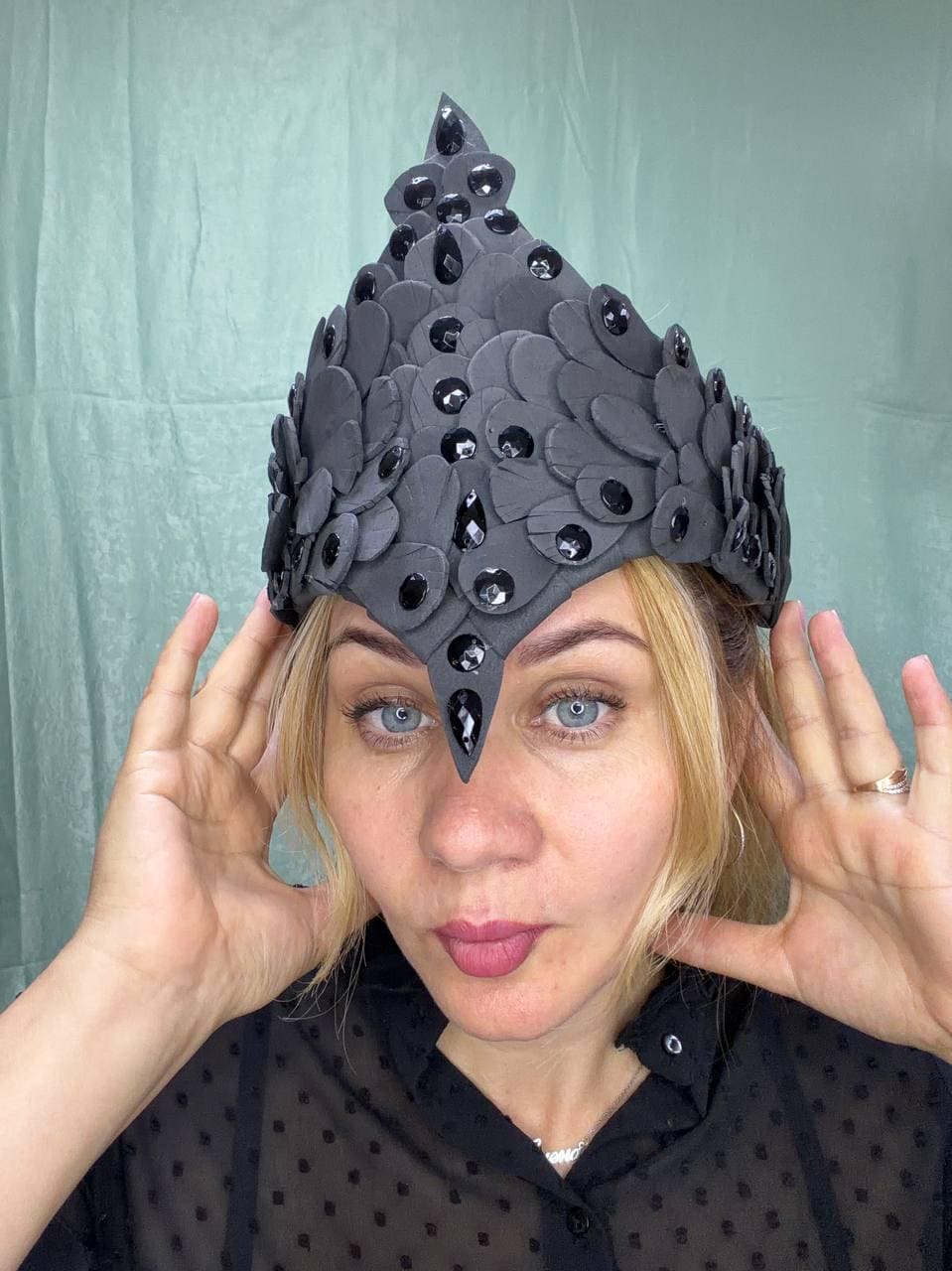 May include: A pointed headpiece constructed from layered, matte black petal-shaped elements. The structure is adorned with numerous faceted, shiny black teardrop-shaped gems arranged in a symmetrical pattern across the surface of the headpiece.