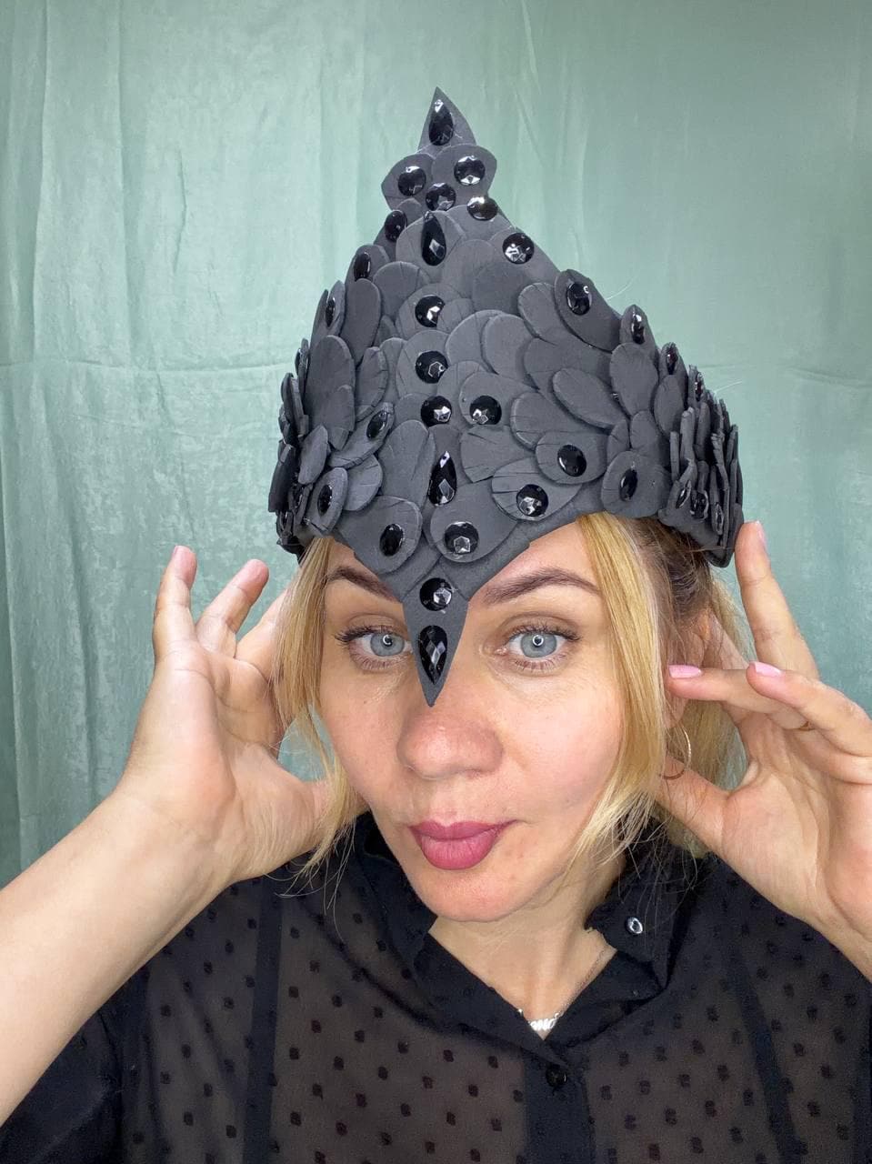 May include: A pointed headpiece constructed from layered matte black petal-shaped elements. The structure is adorned with numerous faceted black crystals arranged in vertical and scattered patterns across the surface, creating a textured appearance.