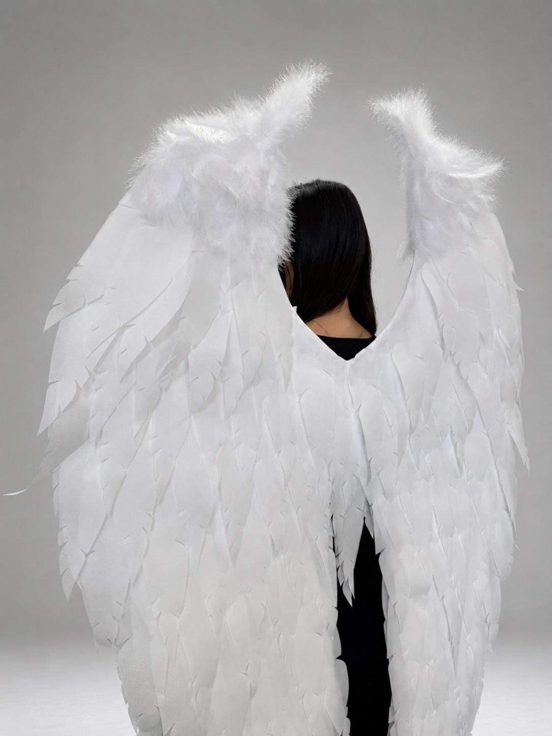 May include: Large white angel wings featuring layered, feather-like cutouts and a fluffy, textured top section. The wings are designed to be worn on the back, displaying a wide, expansive shape with pointed tips and a clean, bright white finish.