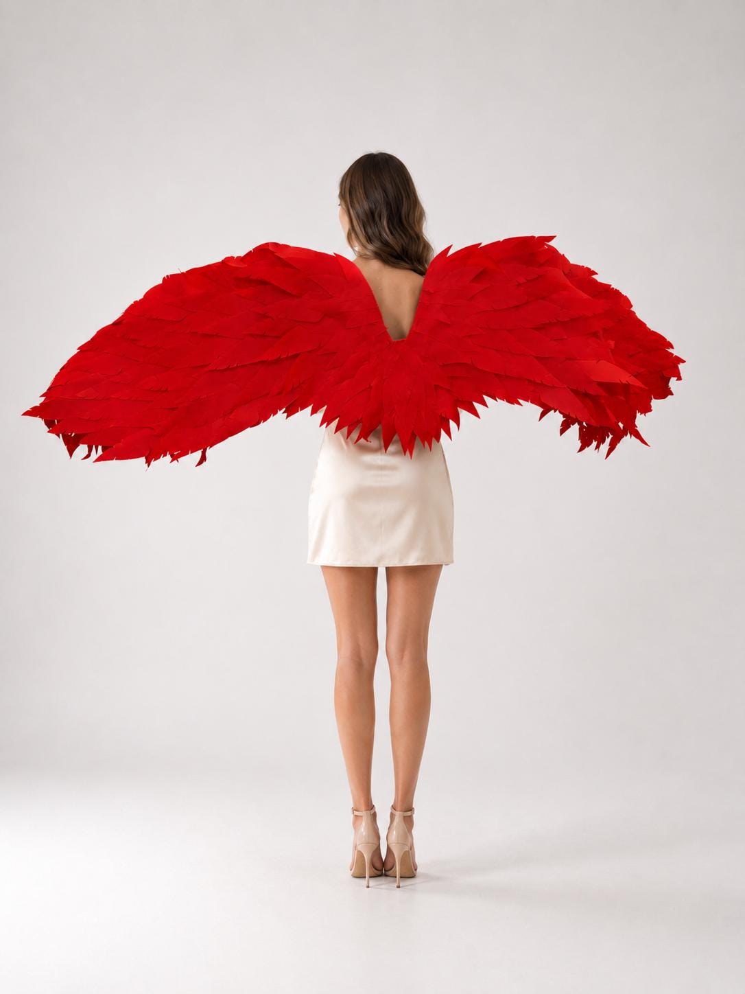 May include: A pair of large, vibrant red wings featuring layered, pointed feather-like segments that extend horizontally. The wings are attached to a beige sleeveless dress, creating a striking contrast between the bold red color and the neutral tone.
