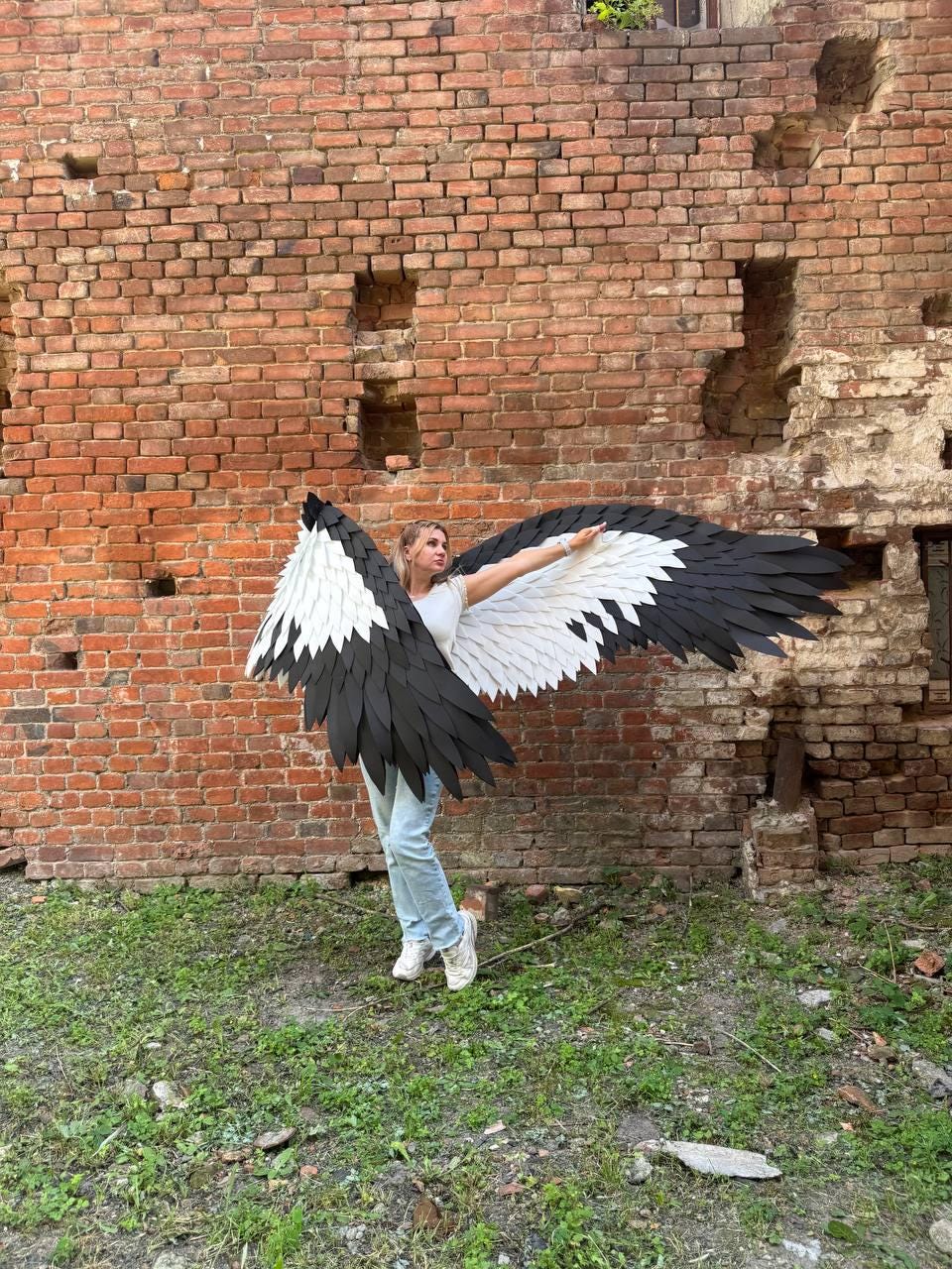 May include: Large, articulated costume wings featuring a layered design of black and white feathers. The wings extend outward, showcasing a gradient pattern where the inner sections are white and the outer primary feathers are solid black.