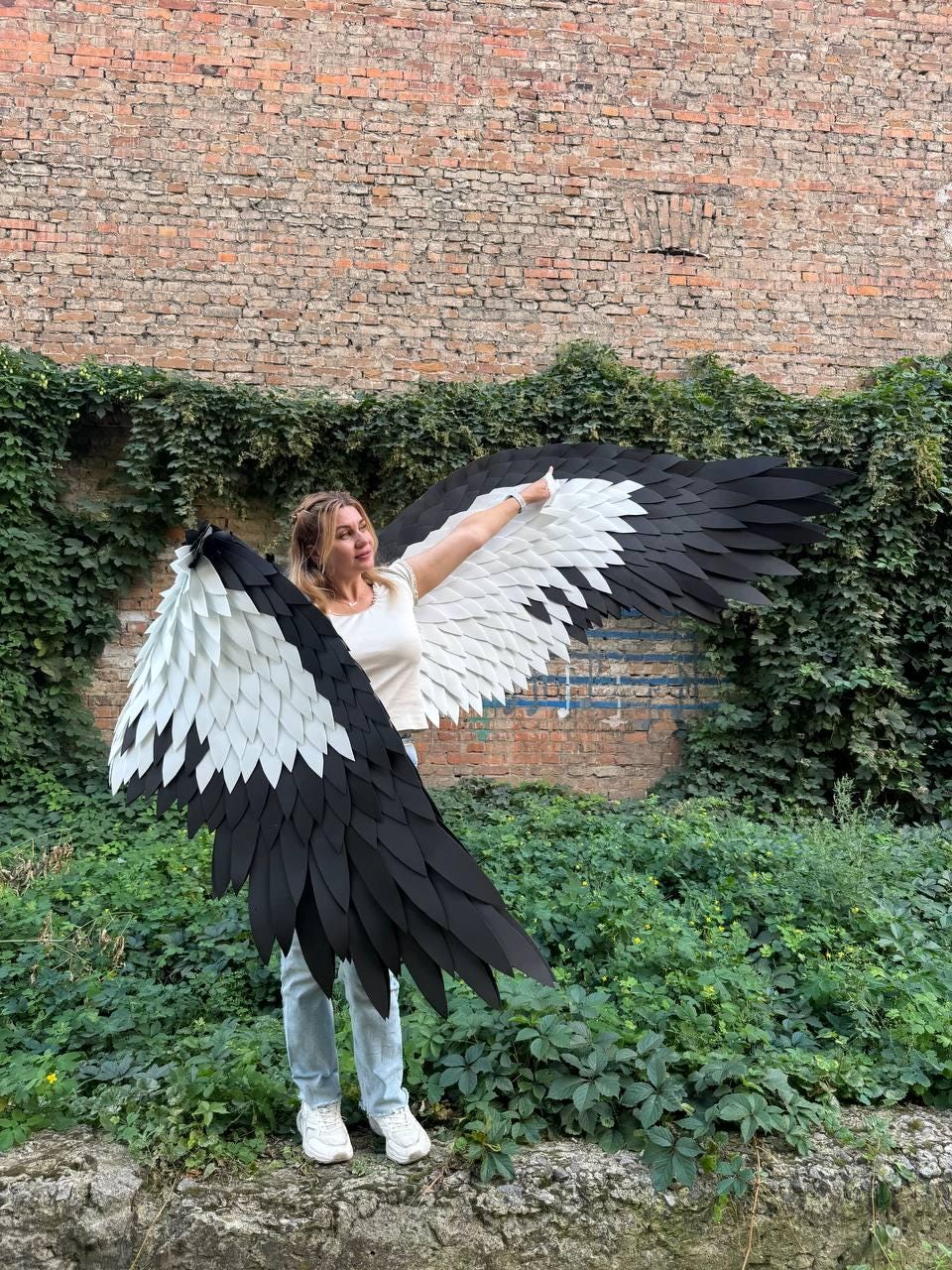 May include: Large wearable wings featuring a layered design of black and white feathers. The wingspan is wide, with white feathers concentrated near the center and black feathers forming the outer edges and tips, creating a high-contrast appearance.