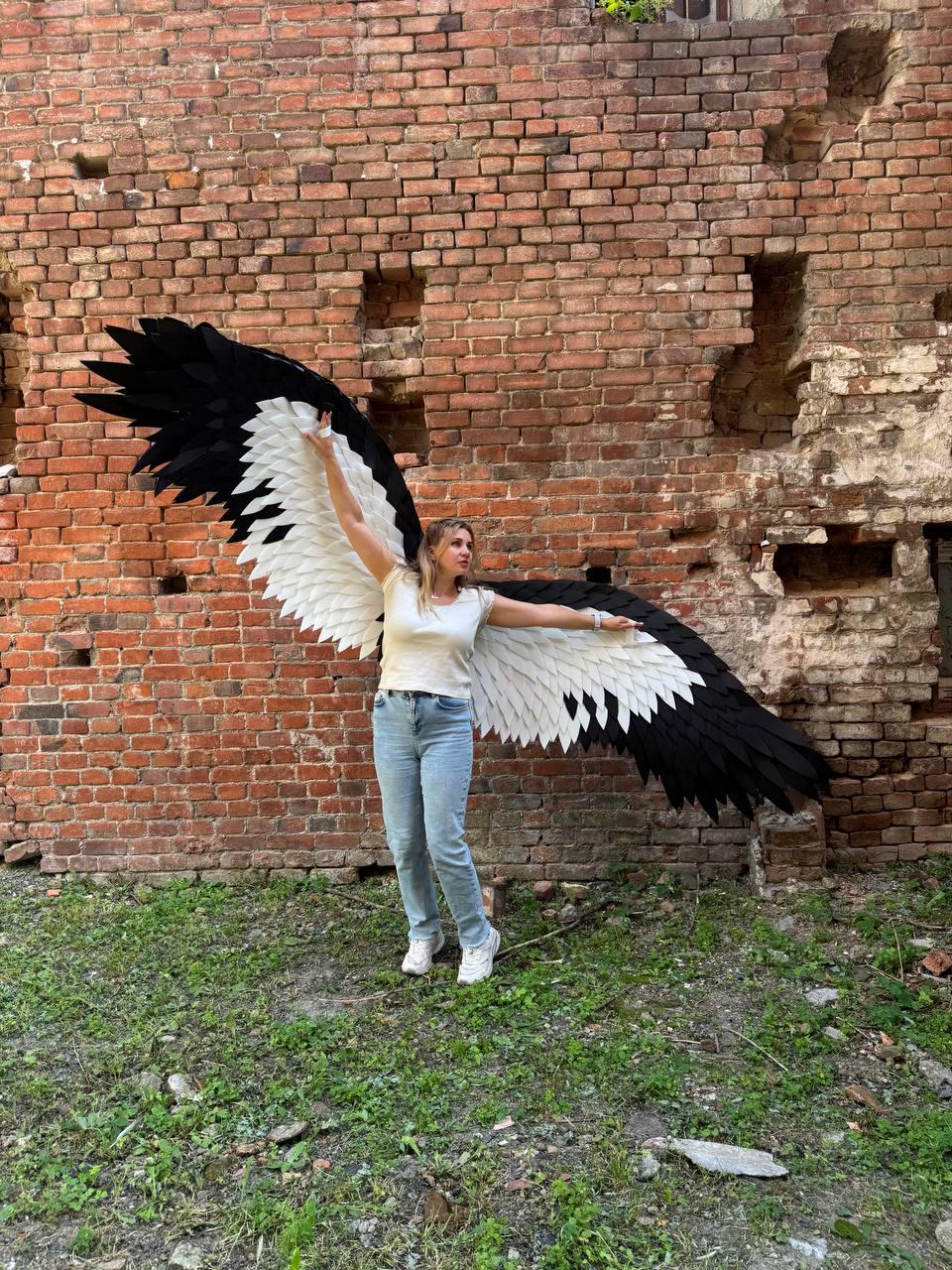 May include: Large decorative wings featuring a layered feather design with a black outer edge and a white inner section. The wings are constructed with individual pointed segments that create a wide, expansive span when fully extended outward.