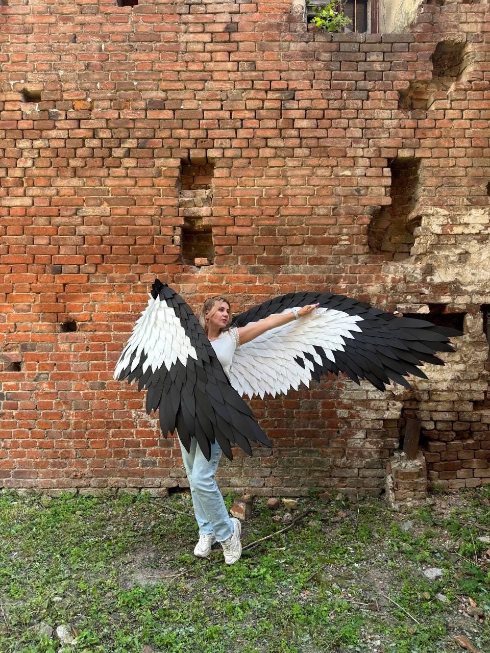 May include: Large, wearable bird-like wings featuring a layered design with black outer feathers and white inner feathers. The wings are constructed with a wide span, showcasing a sharp, pointed shape that mimics the appearance of avian wings.