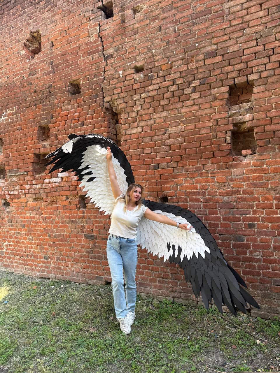 May include: Large decorative wings featuring a layered feather design in black and white. The wings are constructed with individual pointed segments that transition from white at the base to black at the tips, creating a wide, expansive span.