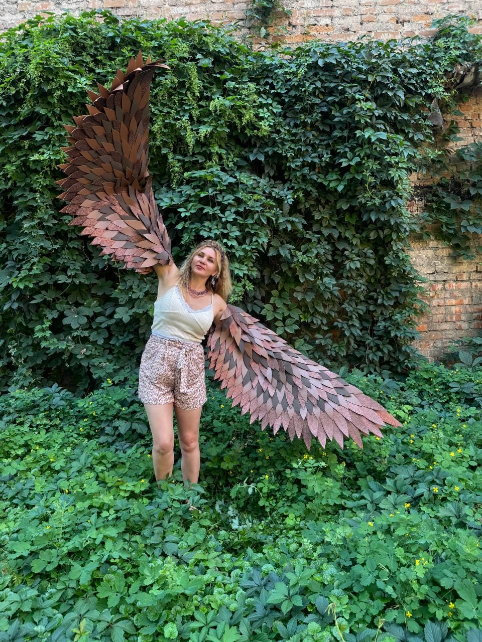 May include: A pair of large, articulated wings featuring layered, dark brown, leaf-shaped feathers. The wings are constructed with a rigid frame and extend outward, showcasing a detailed, textured surface that mimics the appearance of bird plumage.