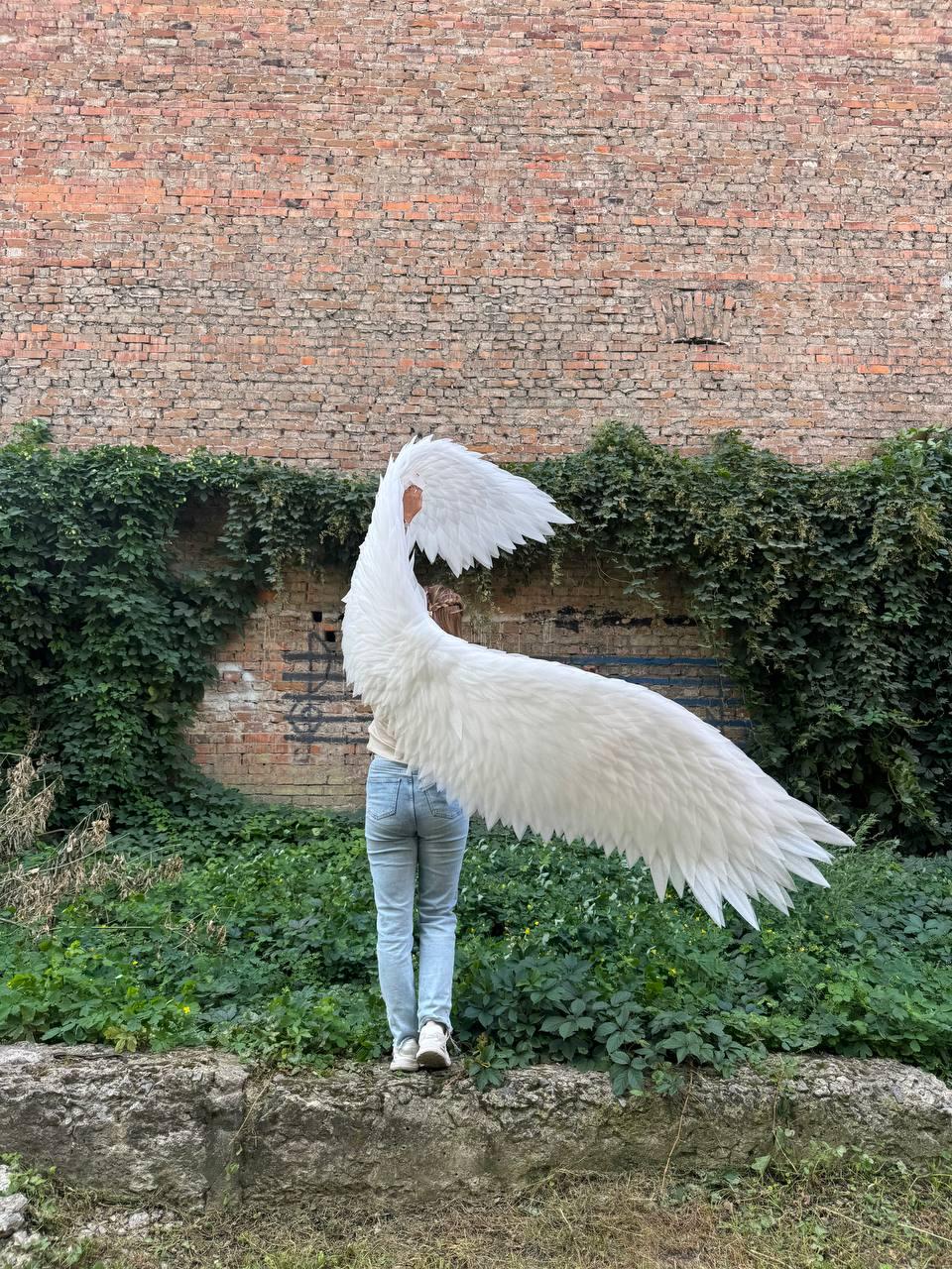 May include: Large, white, articulated angel wings featuring layered, feather-like structures. The wings are expansive, with one section extending upward and the other extending horizontally, showcasing a detailed, pointed plumage design.