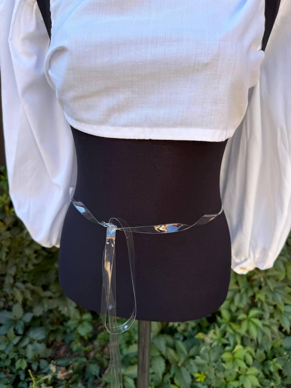 May include: A clear, transparent plastic belt tied in a simple knot at the waist, worn over a white long-sleeved top with voluminous sleeves. The belt is thin, flexible, and smooth, creating a minimalist accent against the white fabric.