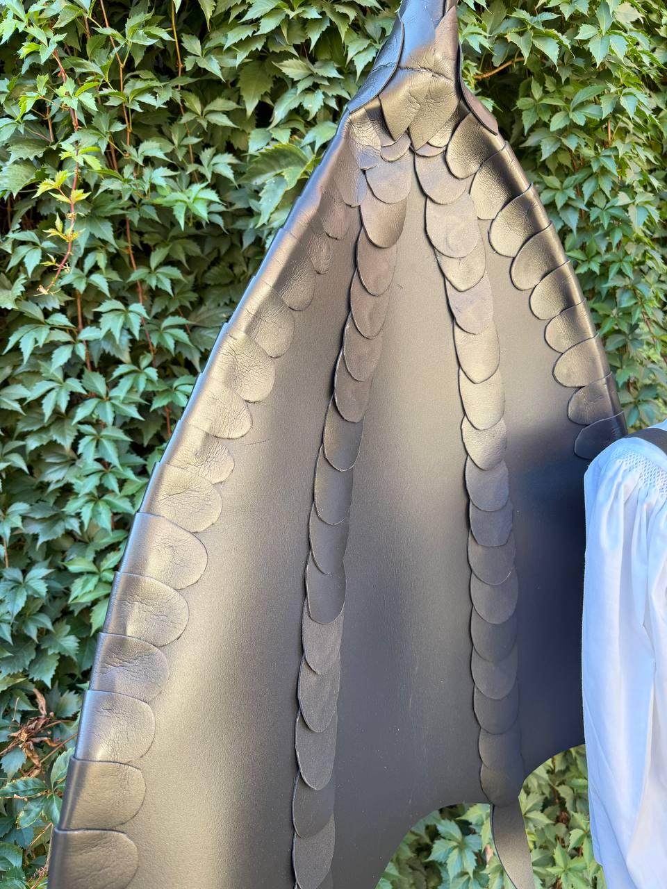May include: A large, black, wing-shaped accessory constructed from smooth material, featuring multiple vertical rows of overlapping, rounded, scale-like segments that extend from the top point down to the base, creating a textured, layered appearance.