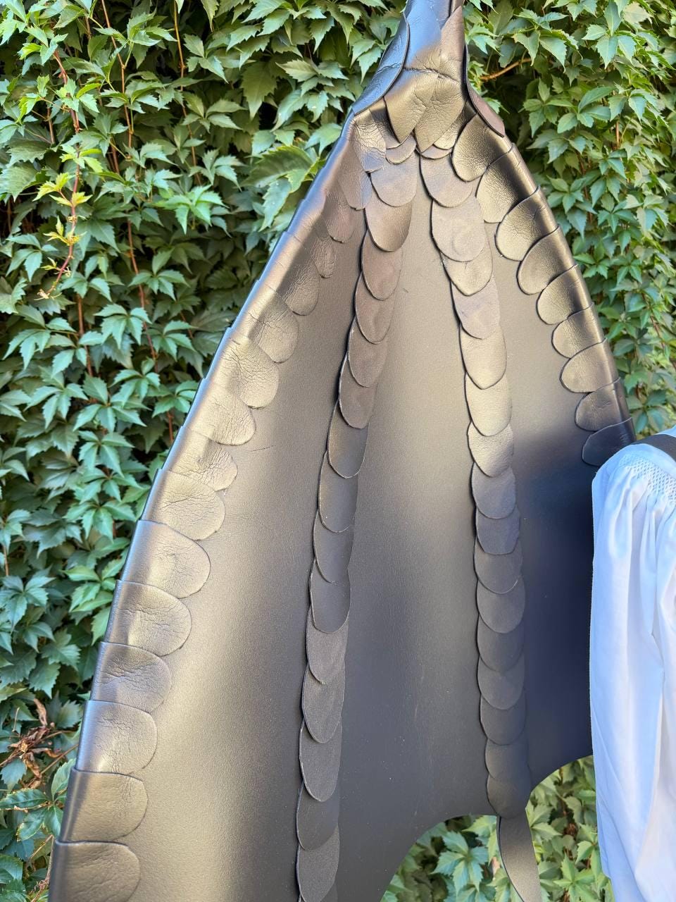 May include: A large, black, wing-shaped accessory constructed from smooth material, featuring multiple vertical rows of overlapping, rounded, scale-like segments that extend from the top point down to the base, creating a textured, layered appearance.