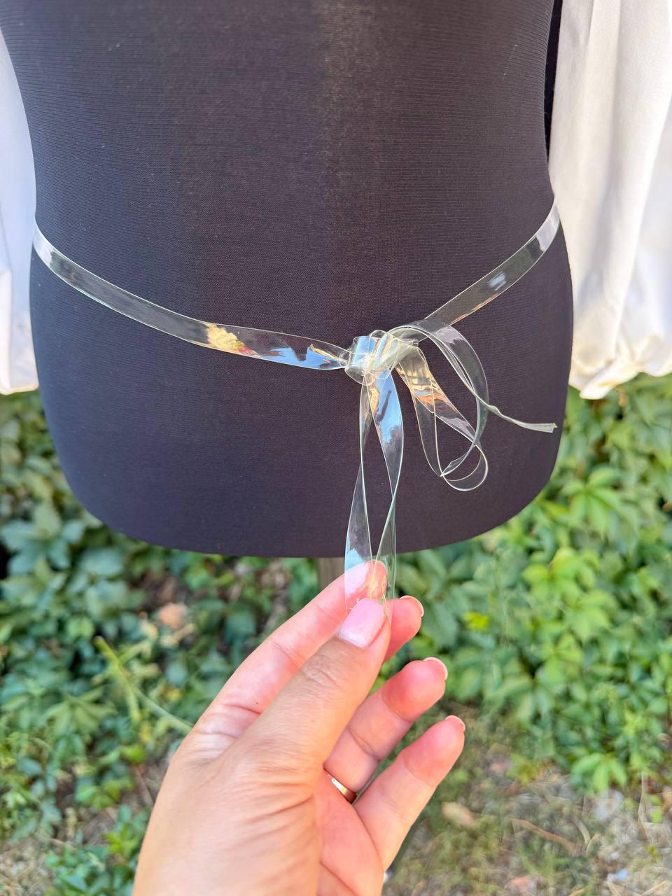 May include: A clear, transparent plastic belt or tie accessory featuring a smooth, flexible material that is tied into a simple knot at the center. The thin, ribbon-like band is designed to wrap around the waist, providing a minimalist look.
