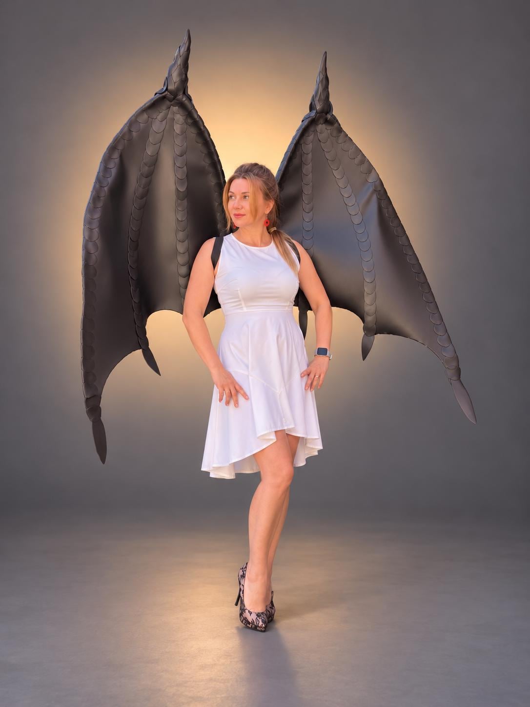 May include: Large, black, articulated dragon-style wings featuring a textured, scale-like pattern. The wings are mounted on a harness structure designed to be worn on the back, extending upwards and outwards with pointed tips and curved edges.