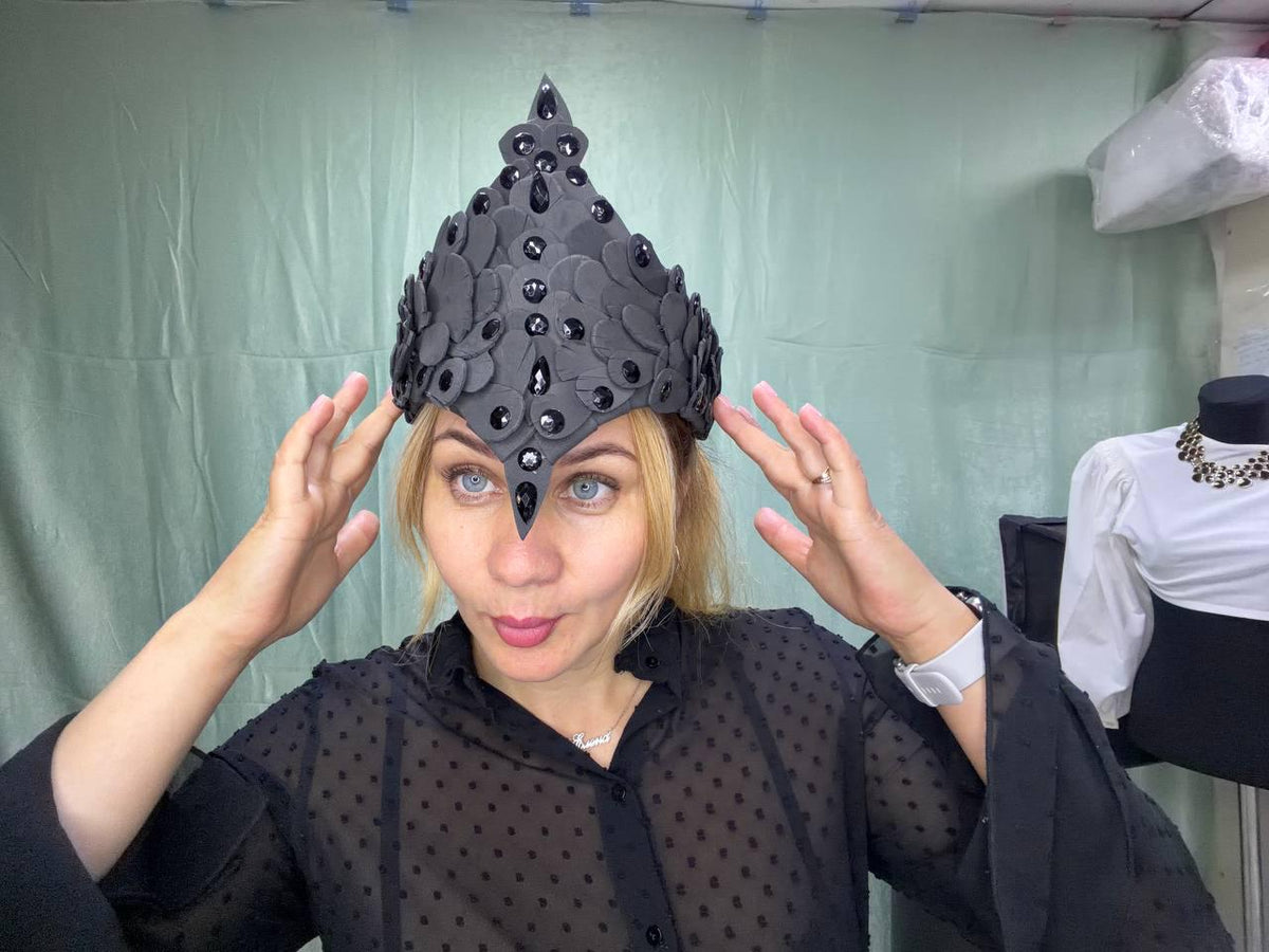 May include: A pointed crown constructed from layered matte black petal-shaped pieces, featuring a central vertical row of faceted black teardrop-shaped gems and additional round black stones embedded throughout the floral-inspired structure.