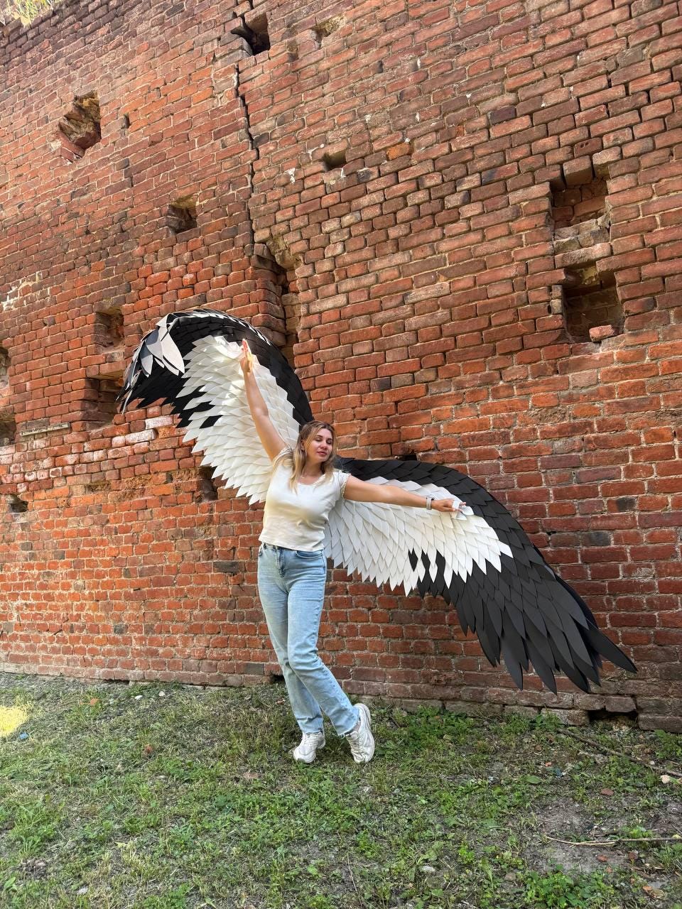 May include: Large, wearable bird-like wings featuring layered, overlapping feathers in a high-contrast black and white color scheme. The wings are designed to be worn on the back, extending outward with a wide span, showcasing detailed feather textures.