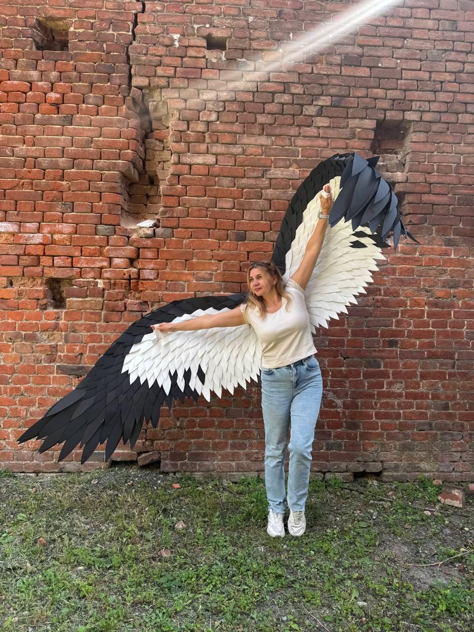 May include: Large, wearable bird wings featuring layered, pointed feathers in a high-contrast black and white color scheme. The wings are constructed with a wide span, showcasing a gradient of white inner feathers transitioning to solid black outer tips.