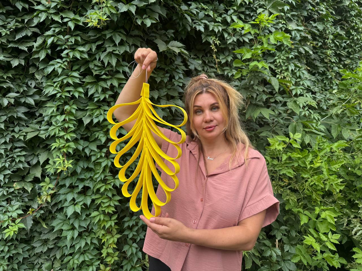May include: A bright yellow decorative hanging ornament shaped like a stylized leaf or feather, constructed from multiple interconnected loops of flat material. The ornament features a pointed top with a thin string loop for suspension and a symmetrical arrangement of curved, elongated yellow segments.