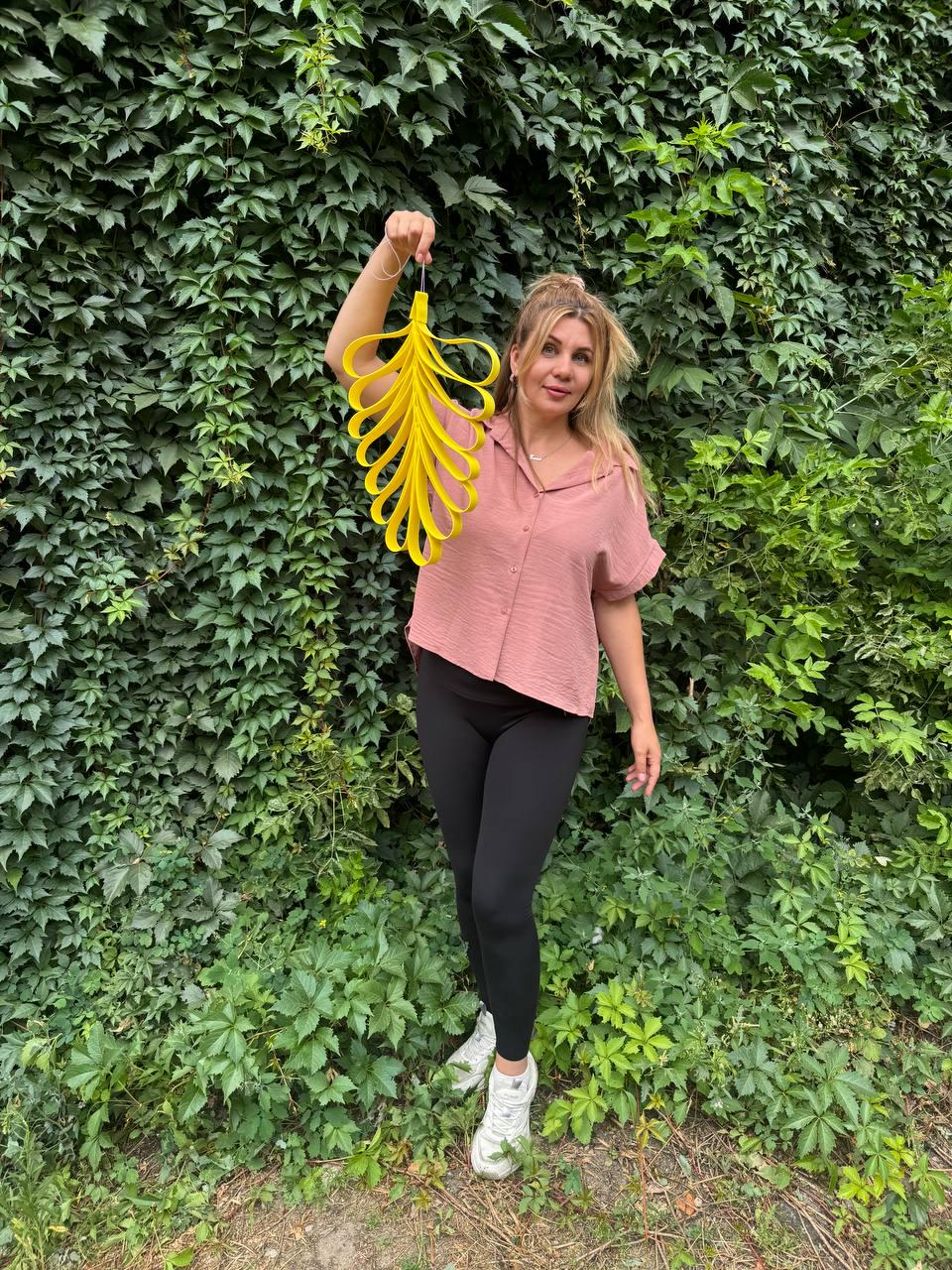 May include: A bright yellow decorative hanging ornament shaped like a stylized leaf or feather, constructed from multiple interconnected loops of flat material, suspended from a thin string loop at the top, showcasing a vibrant and symmetrical design.
