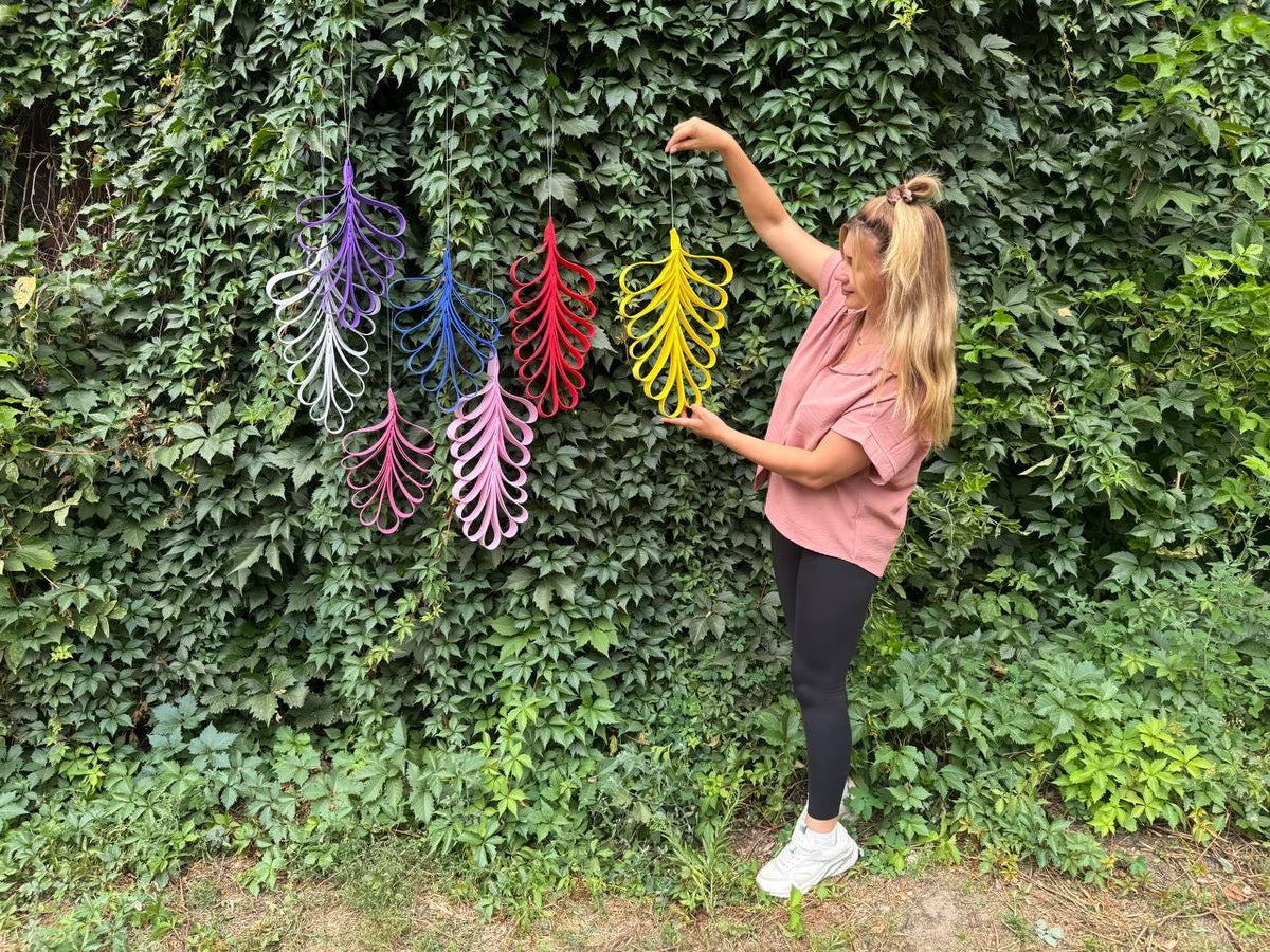 May include: A collection of six hanging leaf-shaped ornaments crafted from looped strips of material. The ornaments are displayed in vibrant colors including purple, white, blue, red, pink, and yellow, each suspended by a thin string.