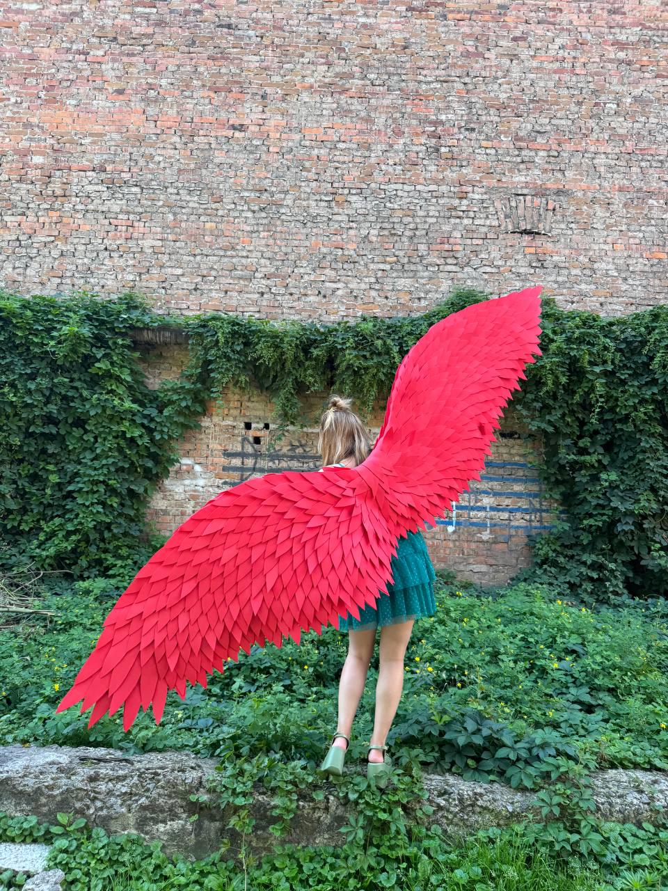 May include: A pair of large, vibrant red wings featuring layered, feather-like segments. The wings are expansive and extend horizontally, showcasing a detailed, textured design with pointed tips. The structure is lightweight and articulated.