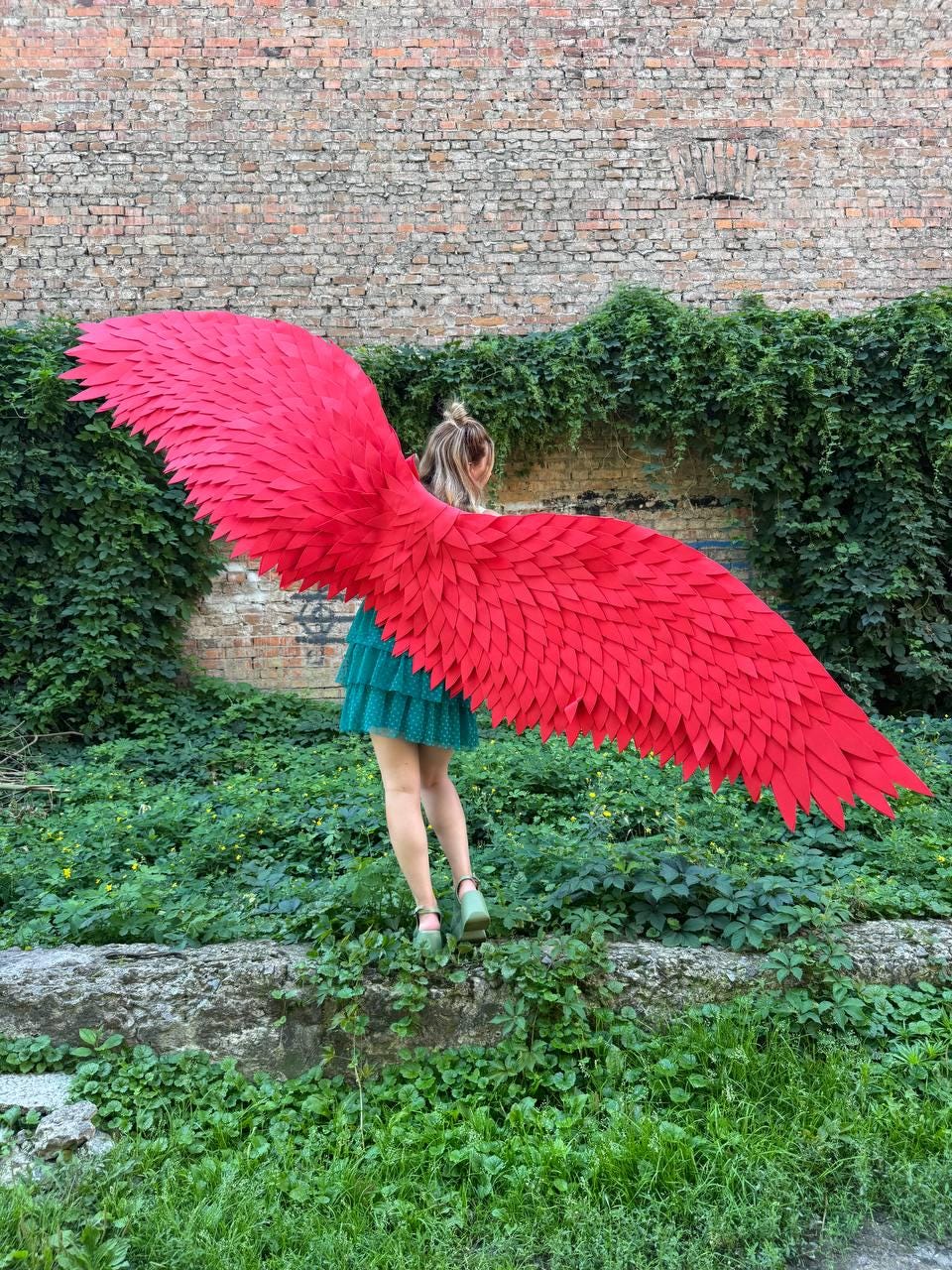May include: Large, vibrant red wings constructed from numerous layered, feather-shaped pieces. The wings extend horizontally, showcasing a detailed, textured surface with a pointed, wing-like silhouette. The structure is lightweight and expansive.