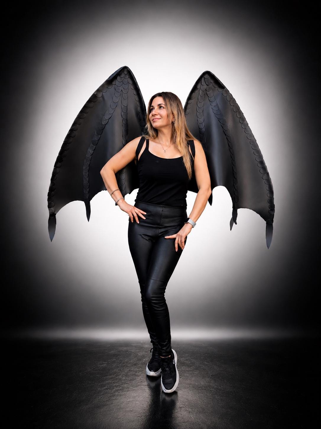 May include: Large black dragon-style wings featuring a detailed scale pattern along the edges. The wings are constructed with a structured frame and are worn as a backpack accessory, extending outward with pointed tips and a smooth matte finish.