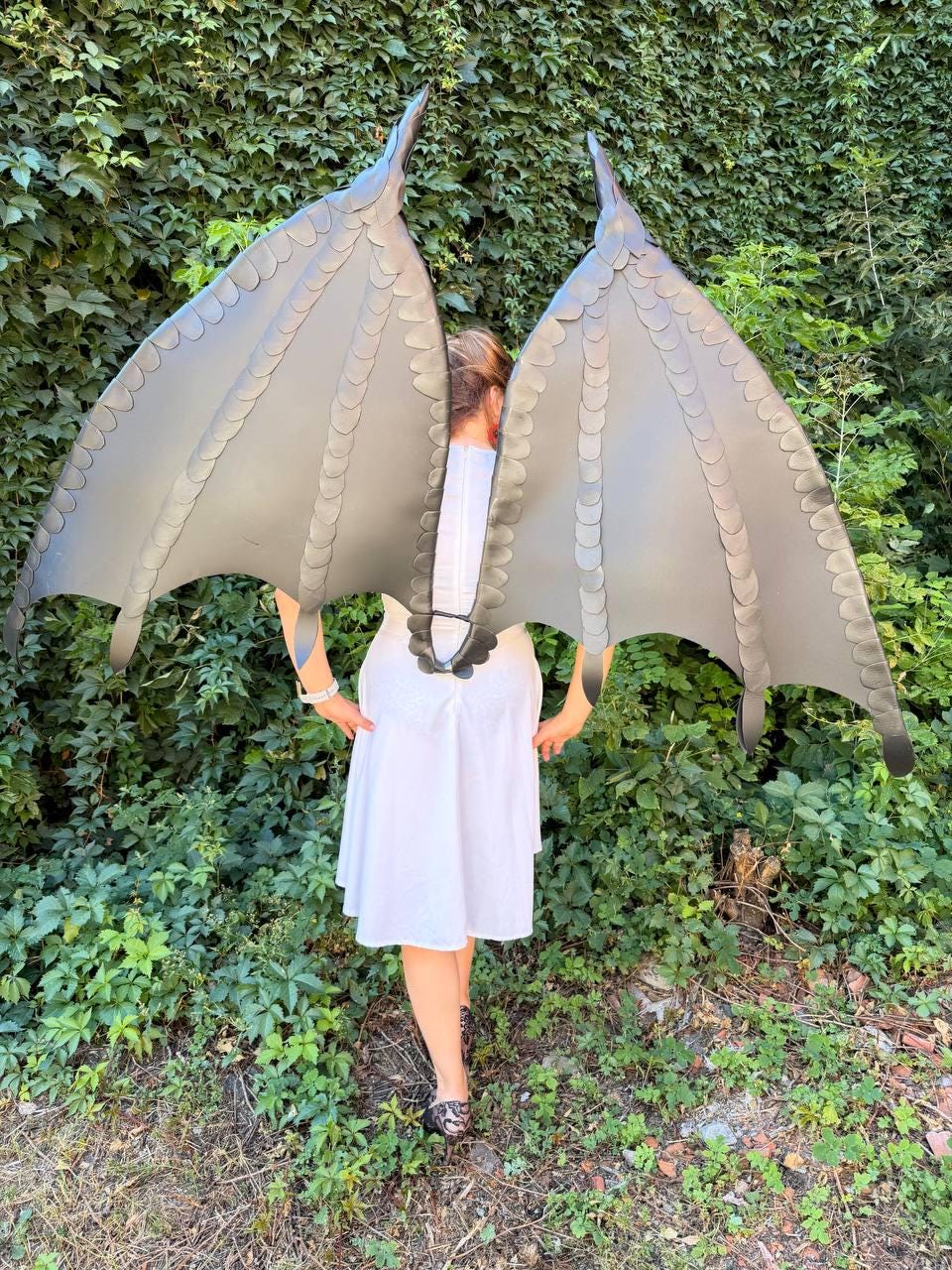 May include: A pair of large, dark gray dragon wings featuring a structured, scale-like pattern along the edges and ribs. The wings are attached to a central harness piece, displaying a wide, expansive span with pointed tips and curved, bat-like membranes.